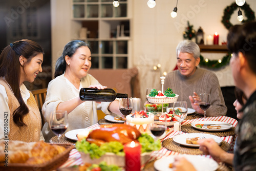 Asian senior older woman celebrating christmas with family cousin in house party while attractive elderly parent pour and toast wine in a glass for Thanksgiving, Xmas Eve and New Year on dining table
