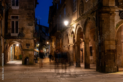 Little Rua do Vilar street with historic residential houses and picturesque passages in the center of Santiago de Compostela at night, a group of people passing by