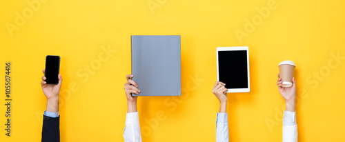 Hands raising up and holding office supplies including tablet computer, file folder, coffee cup and mobile phone isolated on yellow color banner background