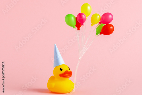 Cute yellow rubber duck with birthday hat and air balloons on pink background.
