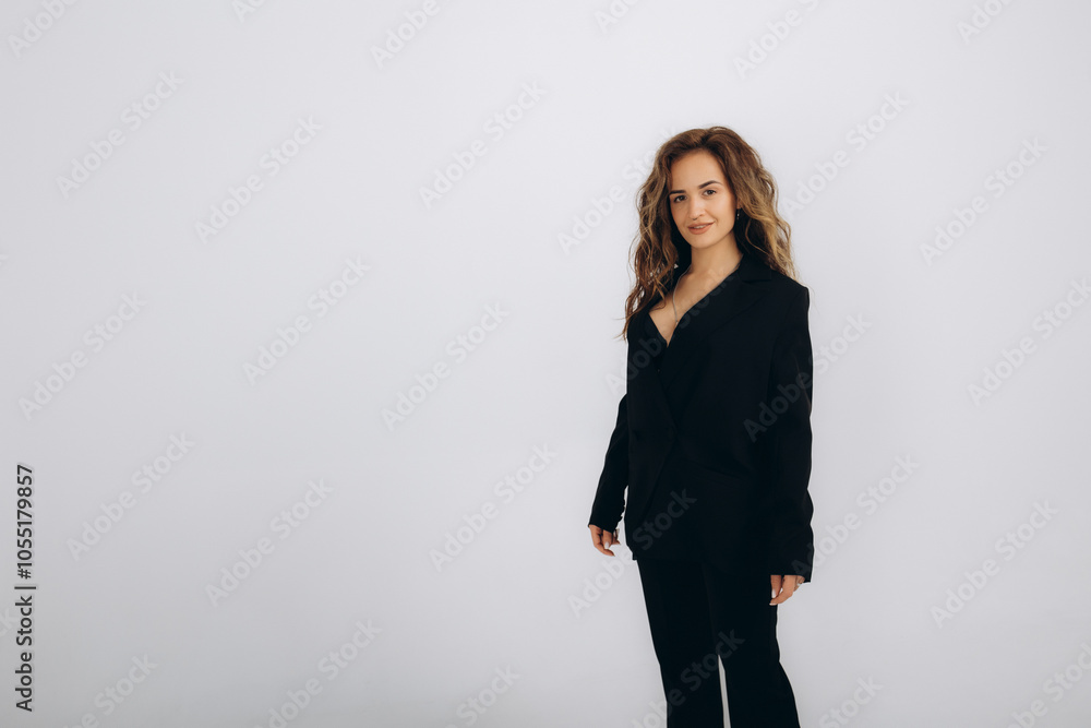 Smiling confident young professional woman with dark hair, wearing black suit and white shirt, standing with arms crossed on light background, copy space Smiling confident young professional woman with dark hair, wearing black suit and white shirt, standing with arms crossed on light background, copy space