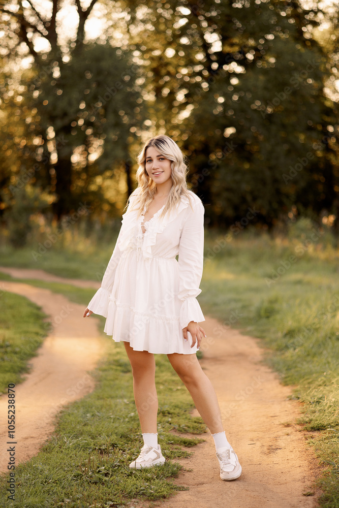 Beautiful young blonde woman in a white dress posing in the park. The concept of a summer fashion collection. Beautiful young blonde woman in a white dress posing in the park. The concept of a summer fashion collection.