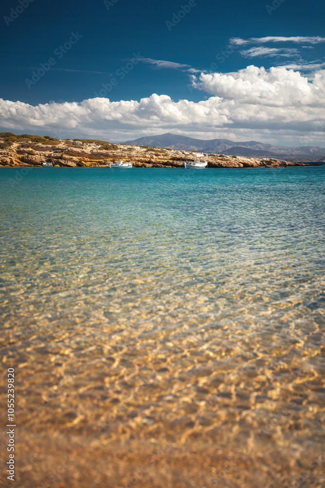 A serene beach on Paros Island, Greece, with golden sands, clear turquoise waters, and gentle waves. Framed by rocky cliffs and lush greenery, it's an idyllic Mediterranean escape under the sun.