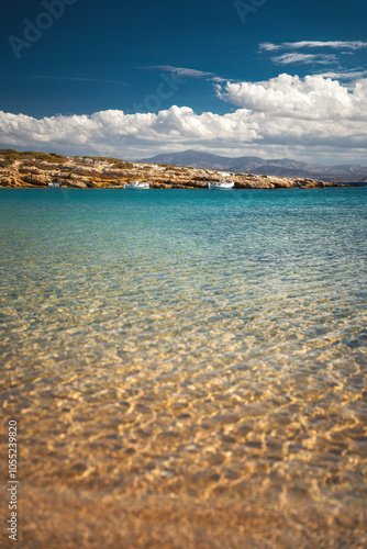 Obraz na płótnie A serene beach on Paros Island, Greece, with golden sands, clear turquoise waters, and gentle waves. Framed by rocky cliffs and lush greenery, it's an idyllic Mediterranean escape under the sun. w salonie