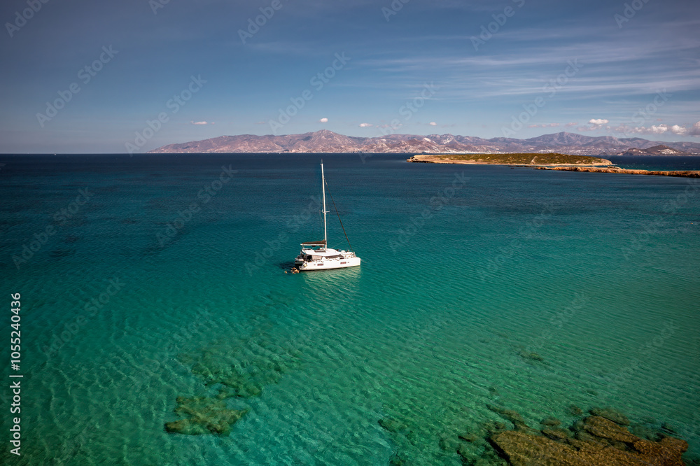 A serene beach on Paros Island, Greece, with golden sands, clear turquoise waters, and gentle waves. Framed by rocky cliffs and lush greenery, it's an idyllic Mediterranean escape under the sun.