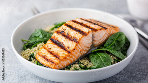 Grilled salmon fillet on quinoa and spinach, plated beautifully in a white bowl, perfect for healthy eating.