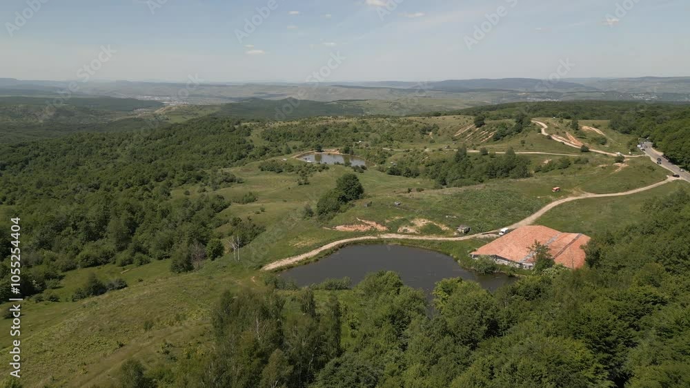 Aerial view of lush green landscape with ponds, a dirt road, and distant mountains under clear sky. Aerial view of lush green landscape with ponds, a dirt road, and distant mountains under clear sky.