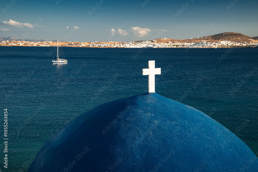A charming blue-domed chapel on Paros Island, Greece, set against the backdrop of the shimmering Aegean Sea. The whitewashed walls, vibrant dome, and surrounding stone path create a picturesque scene