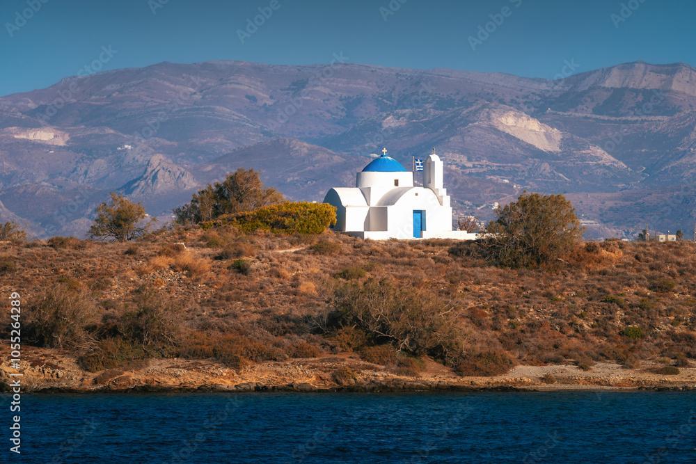 A charming blue-domed chapel on Paros Island, Greece, set against the backdrop of the shimmering Aegean Sea. The whitewashed walls, vibrant dome, and surrounding stone path create a picturesque scene