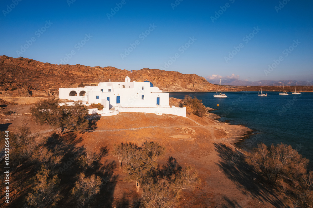 A charming blue-domed chapel on Paros Island, Greece, set against the backdrop of the shimmering Aegean Sea. The whitewashed walls, vibrant dome, and surrounding stone path create a picturesque scene