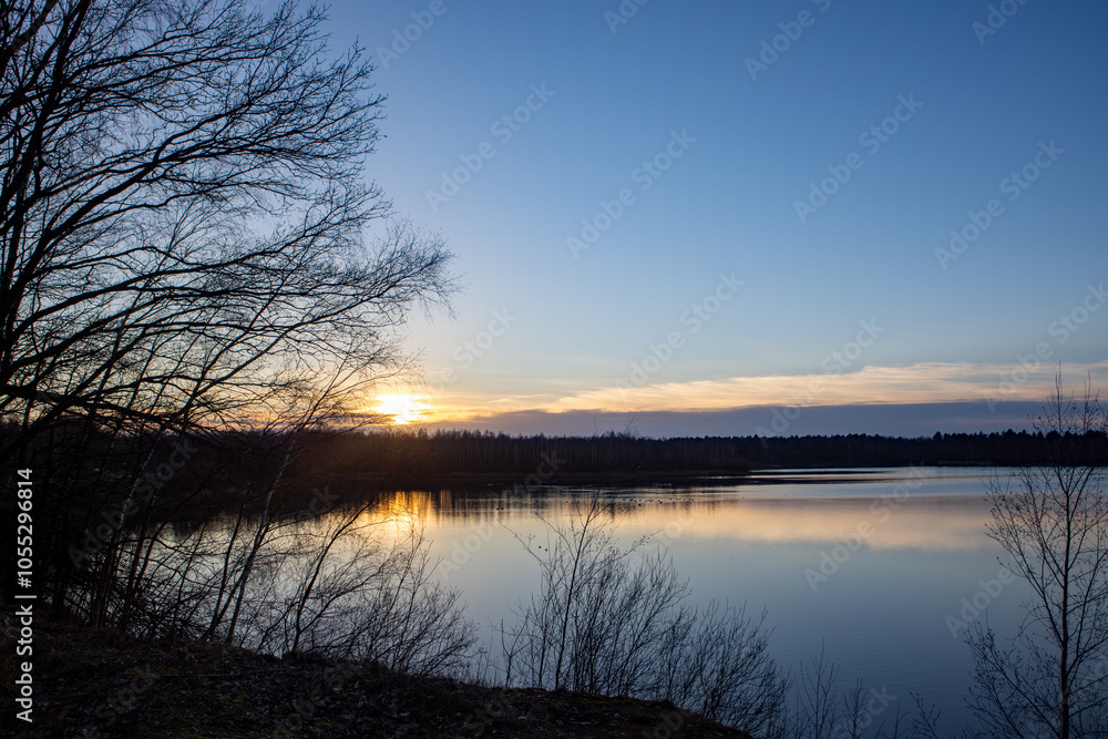 A tranquil sunset with vibrant reflections on a still lake, framed by bare trees and distant mountains A tranquil sunset with vibrant reflections on a still lake, framed by bare trees and distant mountains