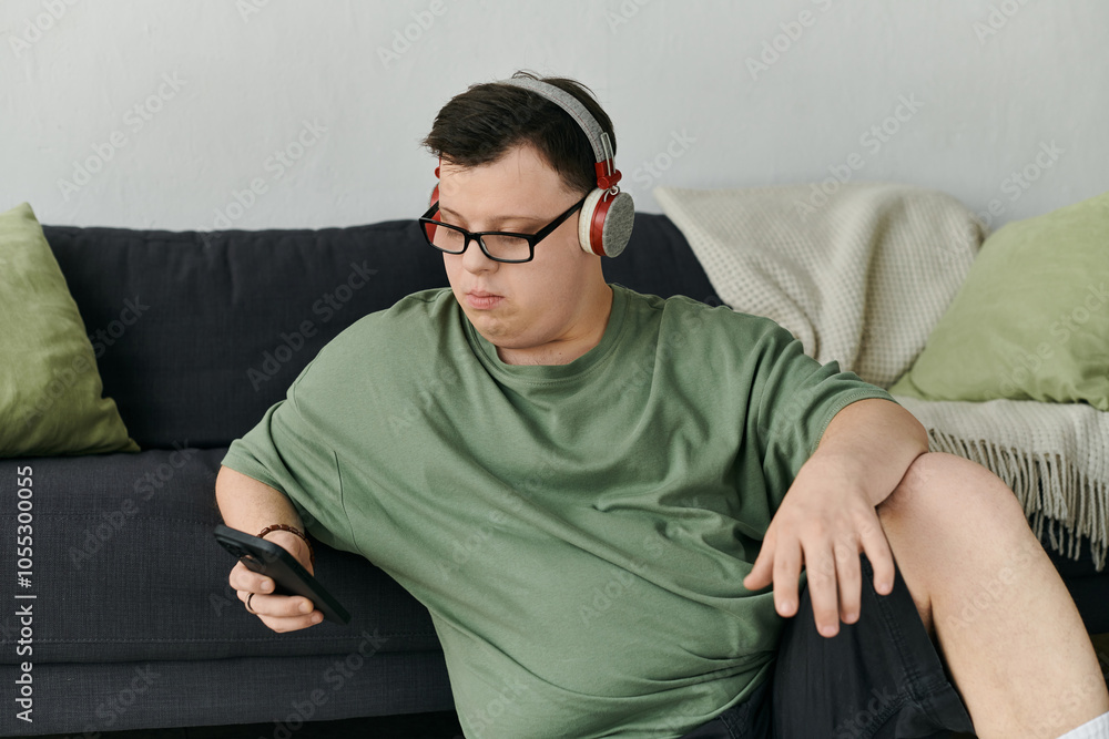 Obraz premium A young man with Down syndrome listens to music while sitting comfortably on a couch.