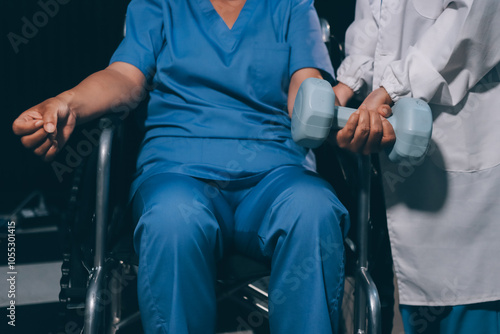 Old woman training with physiotherapist using dumbbells at home. Therapist assisting senior woman with exercises in nursing home. Elderly patient using dumbbells with outstretched arms.