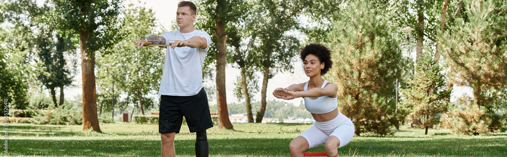 A young woman and tattooed man with a prosthetic leg exercise together in a sunny park. A young woman and tattooed man with a prosthetic leg exercise together in a sunny park.