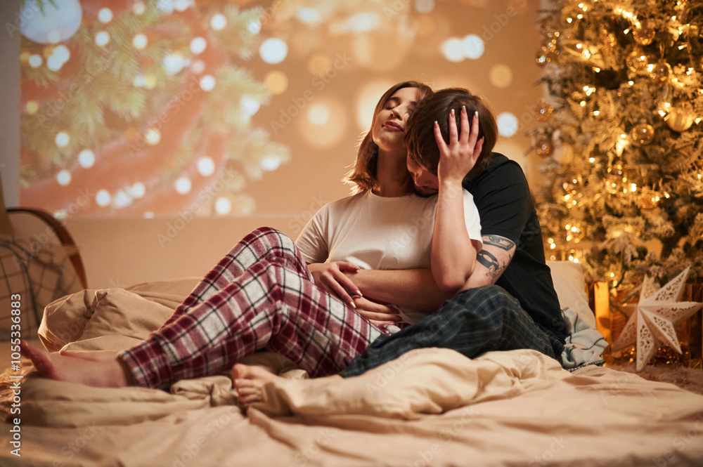 With decorated fir tree. Beautiful young couple indoors, celebrating new year against projector With decorated fir tree. Beautiful young couple indoors, celebrating new year against projector