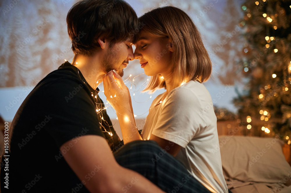 Side view, sitting and embracing. Beautiful young couple indoors, celebrating new year against projector Side view, sitting and embracing. Beautiful young couple indoors, celebrating new year against projector