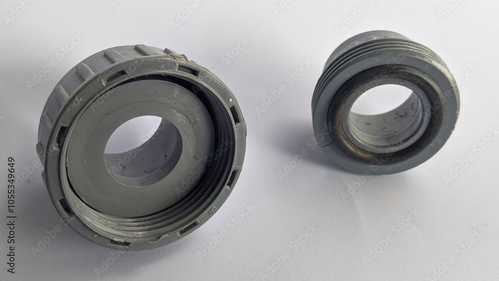 Union Socket PVC Fitting, likely used for connecting pipes together. One fitting has a threaded design on both ends, while the other has a threaded end and a smooth, cylindrical end. Union Socket PVC Fitting, likely used for connecting pipes together. One fitting has a threaded design on both ends, while the other has a threaded end and a smooth, cylindrical end.