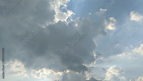 A dramatic sky with a mix of dark gray and light blue clouds. There are streaks of sunlight piercing through the clouds, creating a contrast between light and shadow. photo