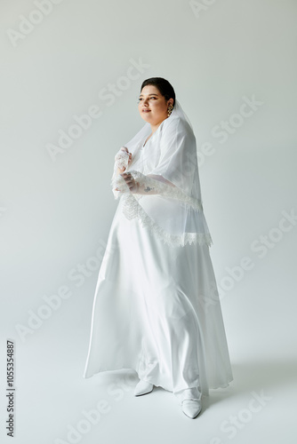 The beautiful bride beams with joy in her exquisite gown and elegant earrings against a minimalist grey background.