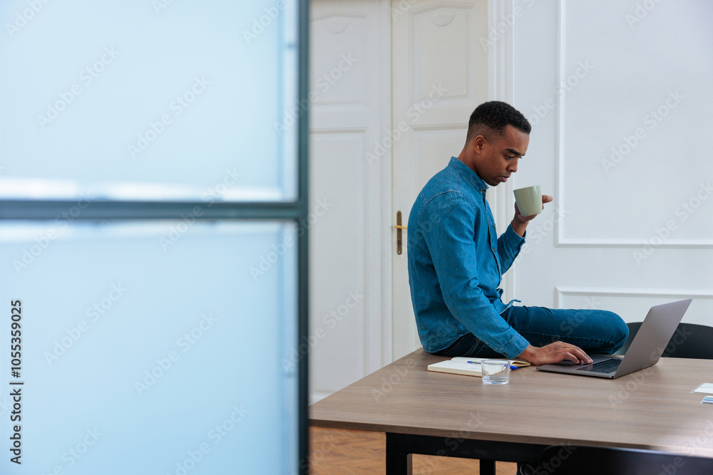 Male employee drinking coffee and looking at his laptop Male employee drinking coffee and looking at his laptop