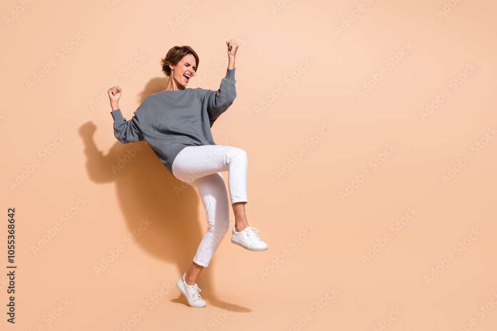 Full length photo of crazy satisfied girl wear pullover white trousers raising up fists shout win bet isolated on beige color background Full length photo of crazy satisfied girl wear pullover white trousers raising up fists shout win bet isolated on beige color background