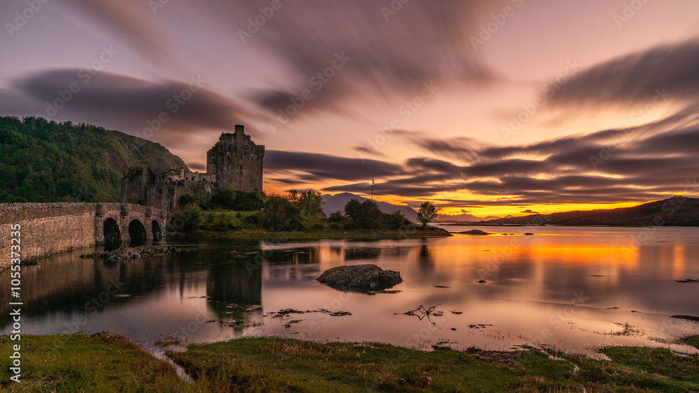 Fototapeta premium Langzeitbelichtung des Eilean Donan Castle, Spiegelung bei Sonnenuntergang im Loch Duich, orange und lila Wolken erzeugen eine mystische Stimmung