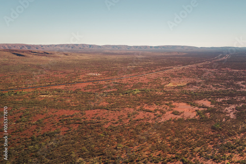 Aerial view of long mine train traversing the vast and barren red earth landscape, Karijini, Australia.