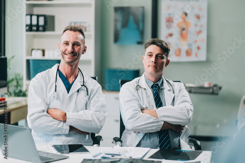 Portrait of two dedicated doctors smiling and looking at camera while holding a tablet and a diary in clinic. Two smiling doctors in white coat working in an office and looking at camera.