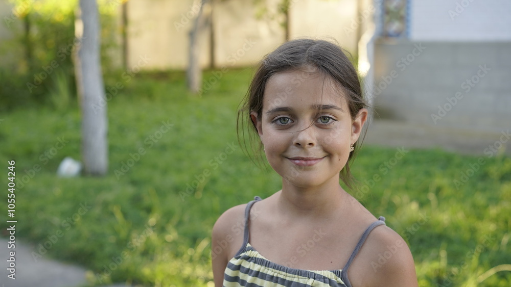 Close-up of a smiling young girl standing outside on a sunny day, with a green, blurred background suggesting a park or yard. Close-up of a smiling young girl standing outside on a sunny day, with a green, blurred background suggesting a park or yard.