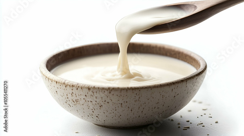 A smooth stream of creamy yogurt being poured into a rustic ceramic bowl, capturing the rich texture and velvety consistency. Perfect for breakfast or as a base for sauces and dips.