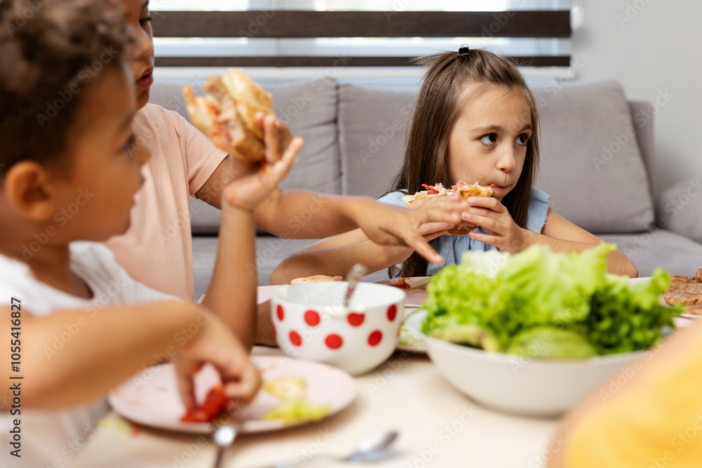 Children eating sandwiches at home around table joyfully Children eating sandwiches at home around table joyfully
