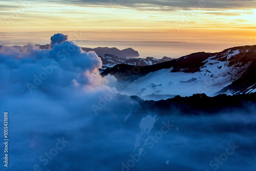 Aerial view of mutnovsky volcano surrounded by clouds and rugged landscape at sunset, Kamchatka, Russia.