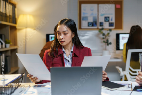 Photography Focused asian businesswoman works late in a dimly lit office, comparing document