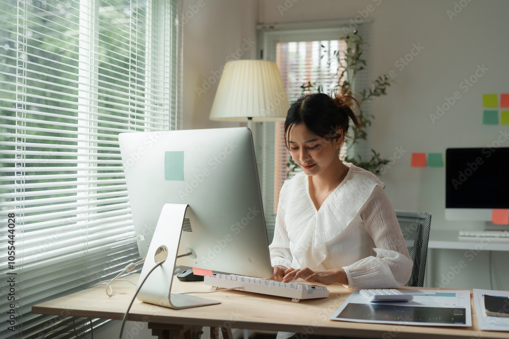 Focused asian businesswoman working from home, typing on a computer keyboard in her bright home office Focused asian businesswoman working from home, typing on a computer keyboard in her bright home office