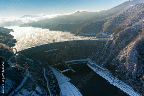 Aerial view of the majestic Neporozhny Sayano Shushenskaya hydro power plant surrounded by snow-covered mountains and a serene river, Khakassia Republic, Russia.