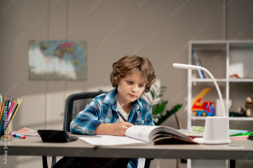 in the children's room a schoolboy in white sweater and a blue checkered shirt at a desk doing homework on his studies writing in a notebook in the children's room a schoolboy in white sweater and a blue checkered shirt at a desk doing homework on his studies writing in a notebook