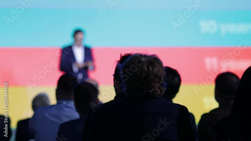 Audience attending a professional conference or business presentation with focus on participants, blurred speaker in background