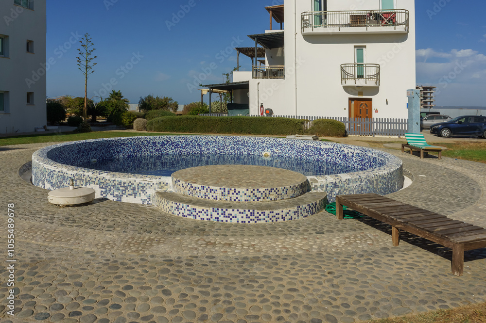 Naklejka premium A serene pool surrounded by quaint buildings and lush landscaping on a bright sunny day.