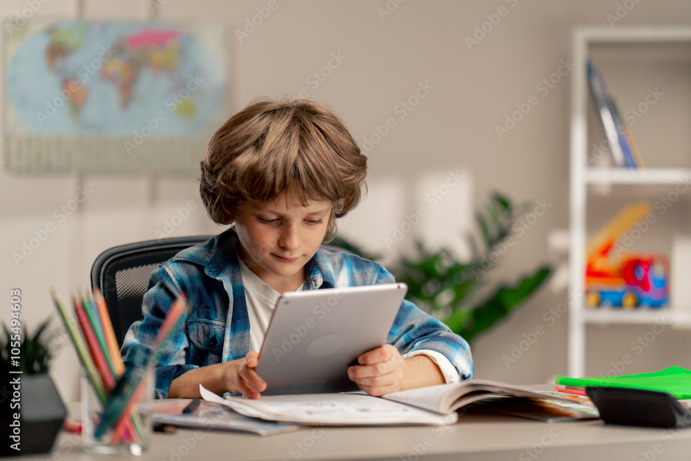 in the children's room a schoolboy in a white sweater and a blue checkered shirt at a desk does homework reads assignments on tablet modern education in the children's room a schoolboy in a white sweater and a blue checkered shirt at a desk does homework reads assignments on tablet modern education