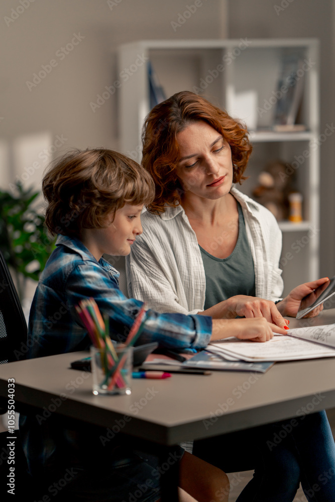 in the children's room a schoolboy in a white sweater and a blue checkered shirt at desk does homework mom explains the task in the children's room a schoolboy in a white sweater and a blue checkered shirt at desk does homework mom explains the task