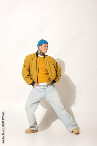 A young man with striking tattoos stands confidently in a yellow sweater and jacket.