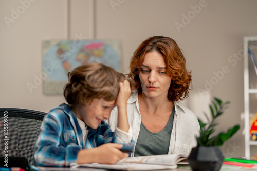 in the children's room a schoolboy in a white sweater and a blue checkered shirt at desk does homework mom explains the task