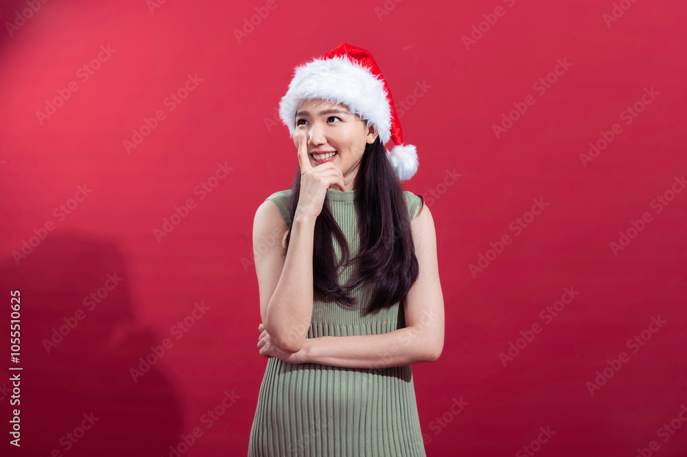 An Asian woman with long black hair, dressed in a green sleeveless outfit, wearing a Santa hat, smiles playfully with one hand on her chin and the other arm crossed, set against a red background An Asian woman with long black hair, dressed in a green sleeveless outfit, wearing a Santa hat, smiles playfully with one hand on her chin and the other arm crossed, set against a red background