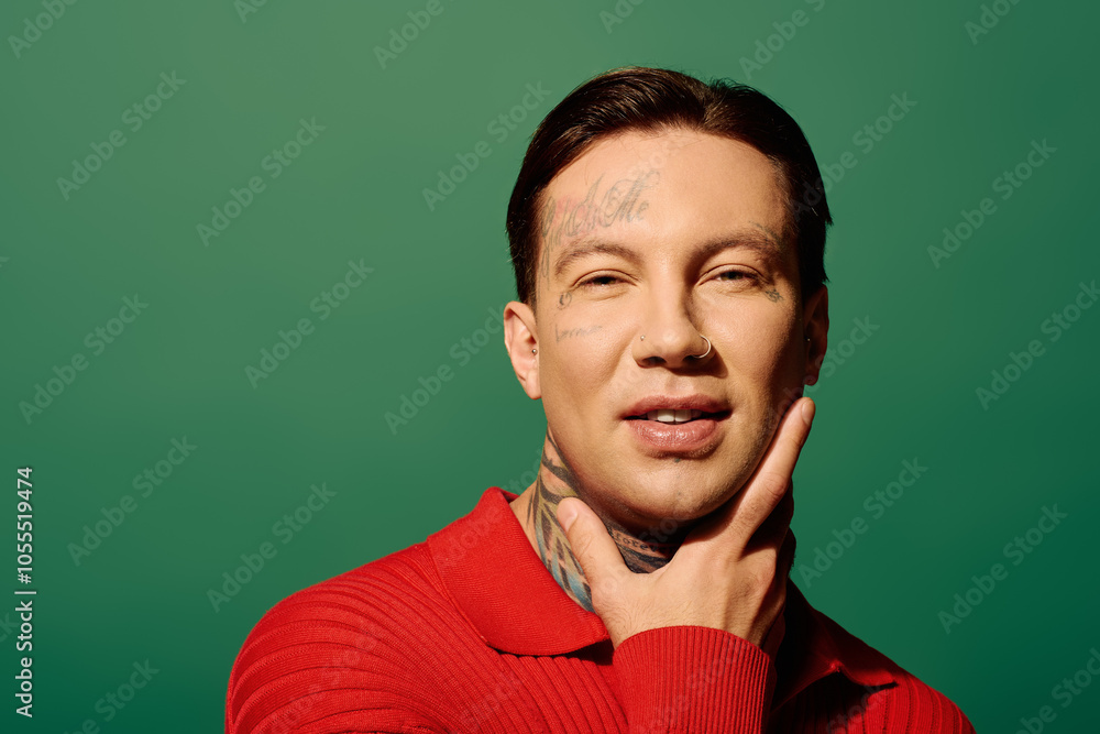 The young man showcases his tattoos while striking a playful pose in front of a bold green backdrop. The young man showcases his tattoos while striking a playful pose in front of a bold green backdrop.