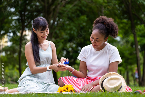 Couple of LGBTQ lesbian people having picnic in the park during summer while putting sunscreen on each other for pride month and marriage equality concept photo