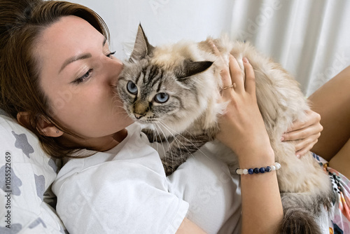 A woman is laying on a bed with a neva masquerade cat on her lap. Close up.