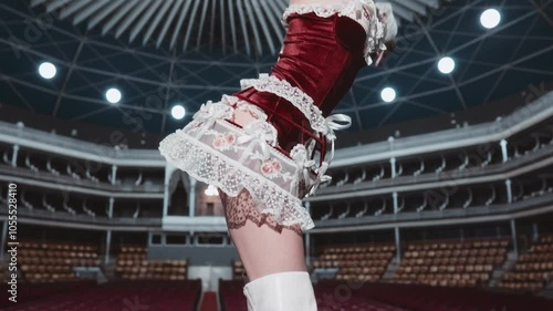 A showgirl in a red and white burlesque costume dances on stage, focusing on the back of her outfit. She wears matching white boots.