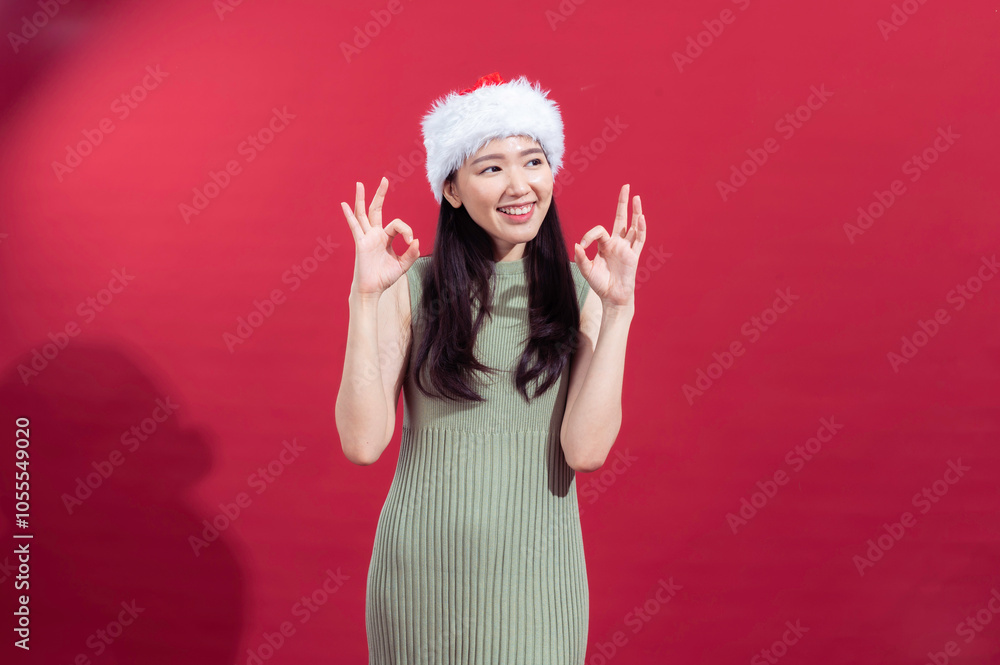 An Asian woman wearing a sleeveless green ribbed dress and a Santa hat is smiling and gesturing the An Asian woman wearing a sleeveless green ribbed dress and a Santa hat is smiling and gesturing the
