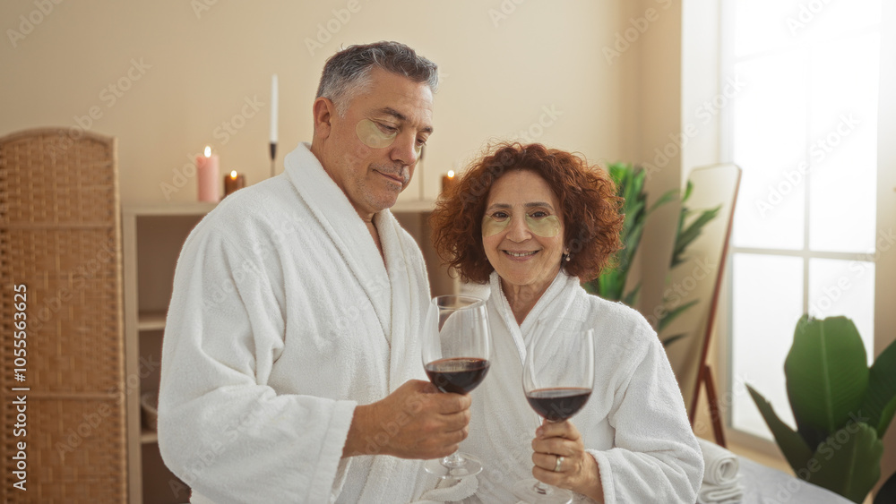 Middle-aged couple wearing bathrobes enjoy a glass of wine at a spa salon in an indoor wellness room with candles and plants creating a relaxing atmosphere Middle-aged couple wearing bathrobes enjoy a glass of wine at a spa salon in an indoor wellness room with candles and plants creating a relaxing atmosphere