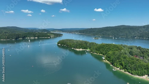 Flying over the lake with a view of the mountains and boats floating on the shore and in the middle of the lake. Beautiful summer colors. Visible islands and small headlands. Mavic 3